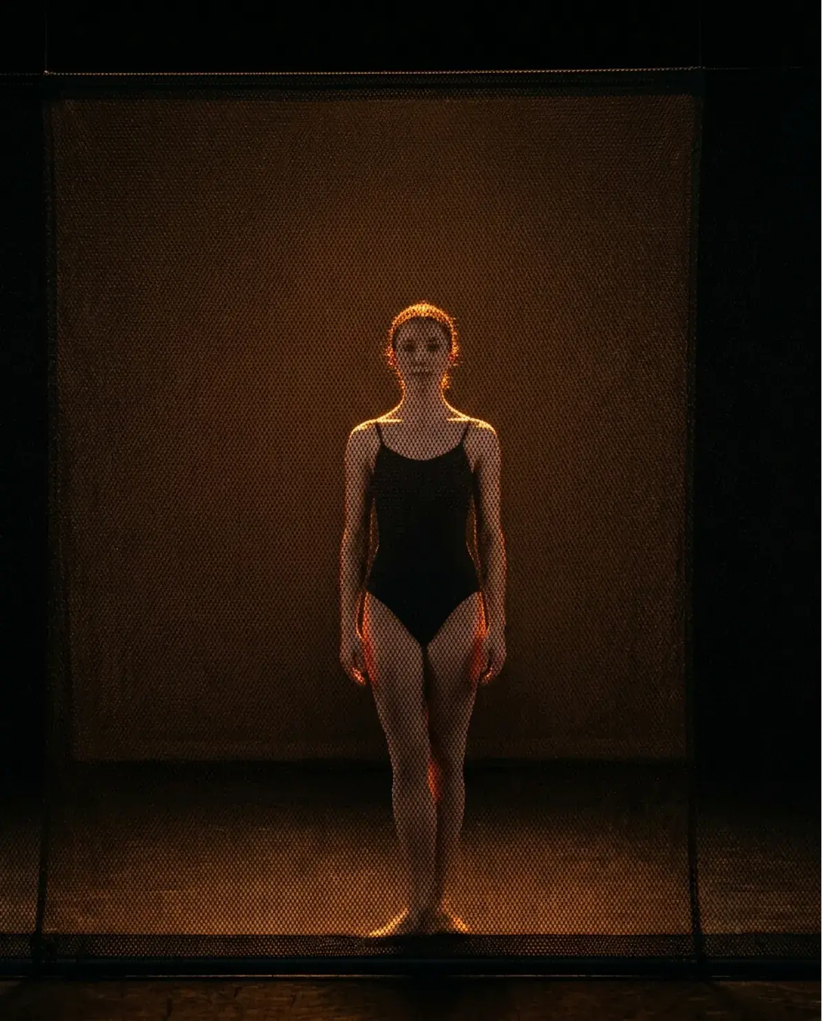 A sharkstooth scrim lit from behind, turning transparent so the performer stands sharply visible through the gauze