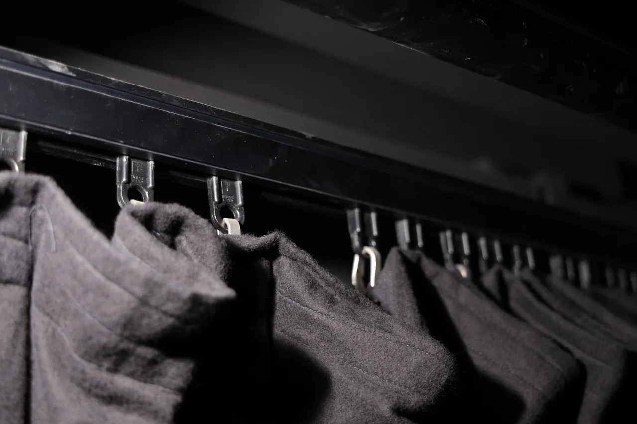Grey wool drapes hanging from track runners on a black curtain track
