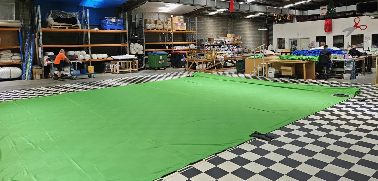 A green-screen chroma cloth laid out on the workshop floor with fabric rolls behind