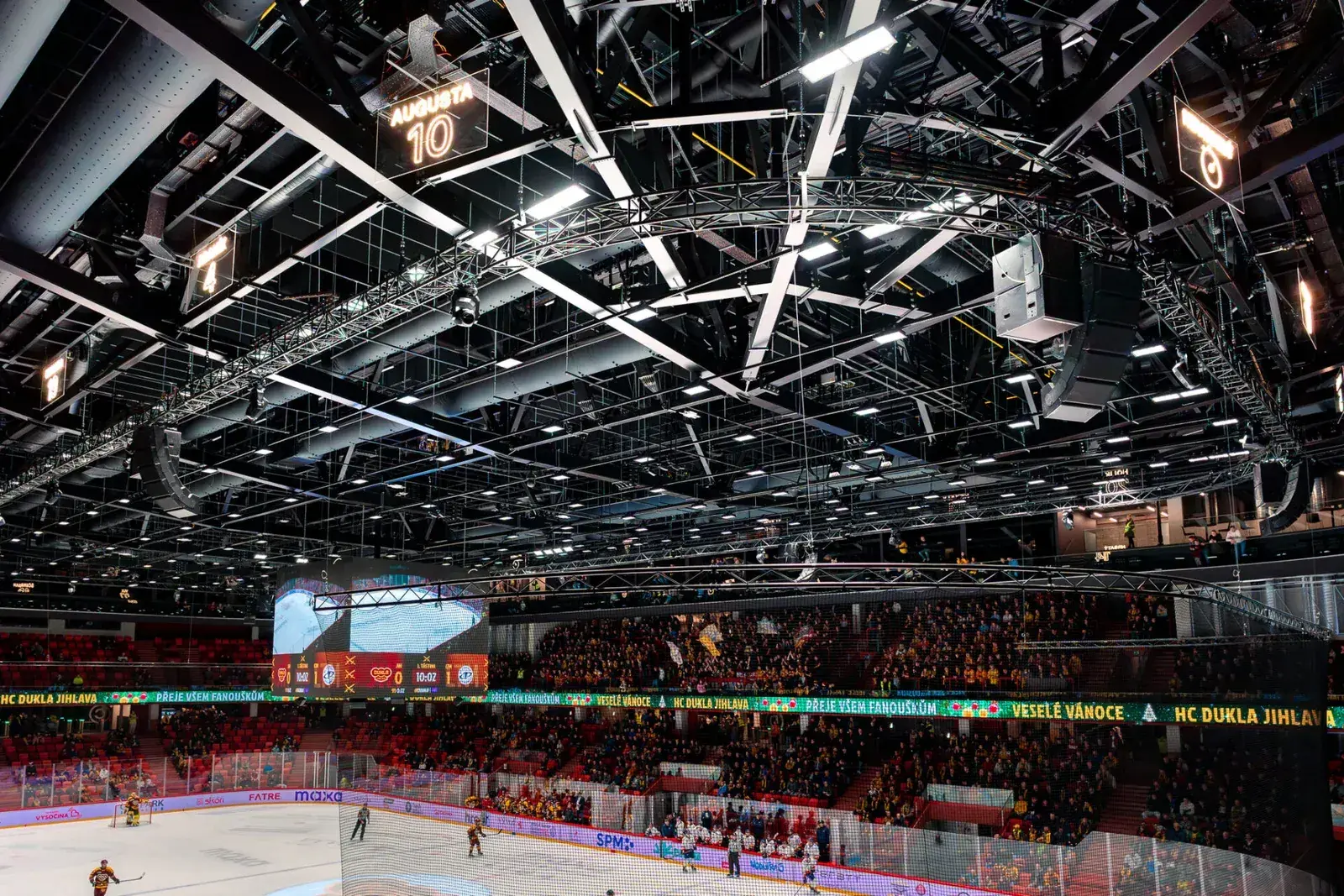 Wide view of an arena roof packed with overhead truss, rigging and flown equipment above a full crowd.