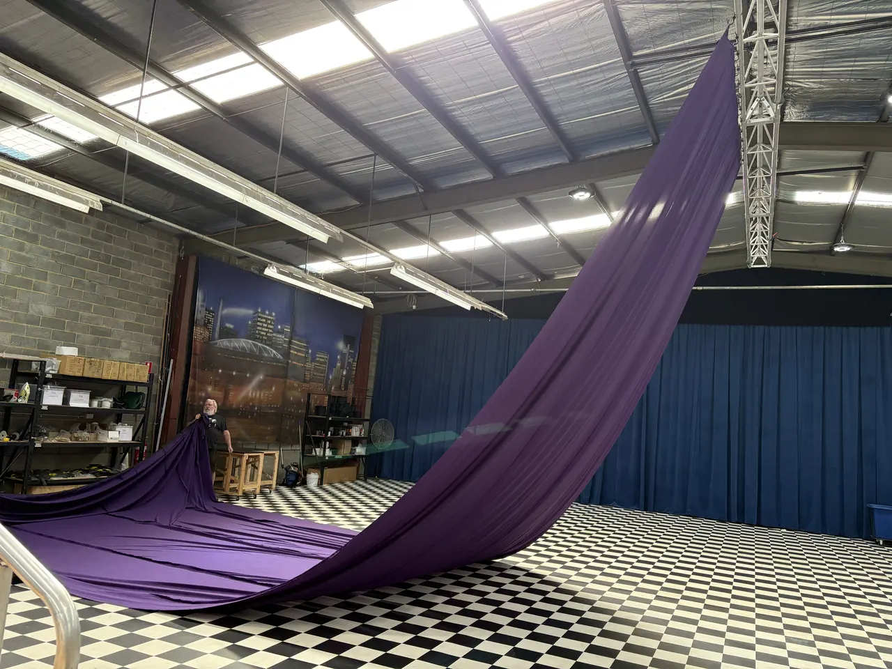A purple roof swag sweeping from the workshop floor up to a truss in the roof during a test hang, with a staff member holding the low end