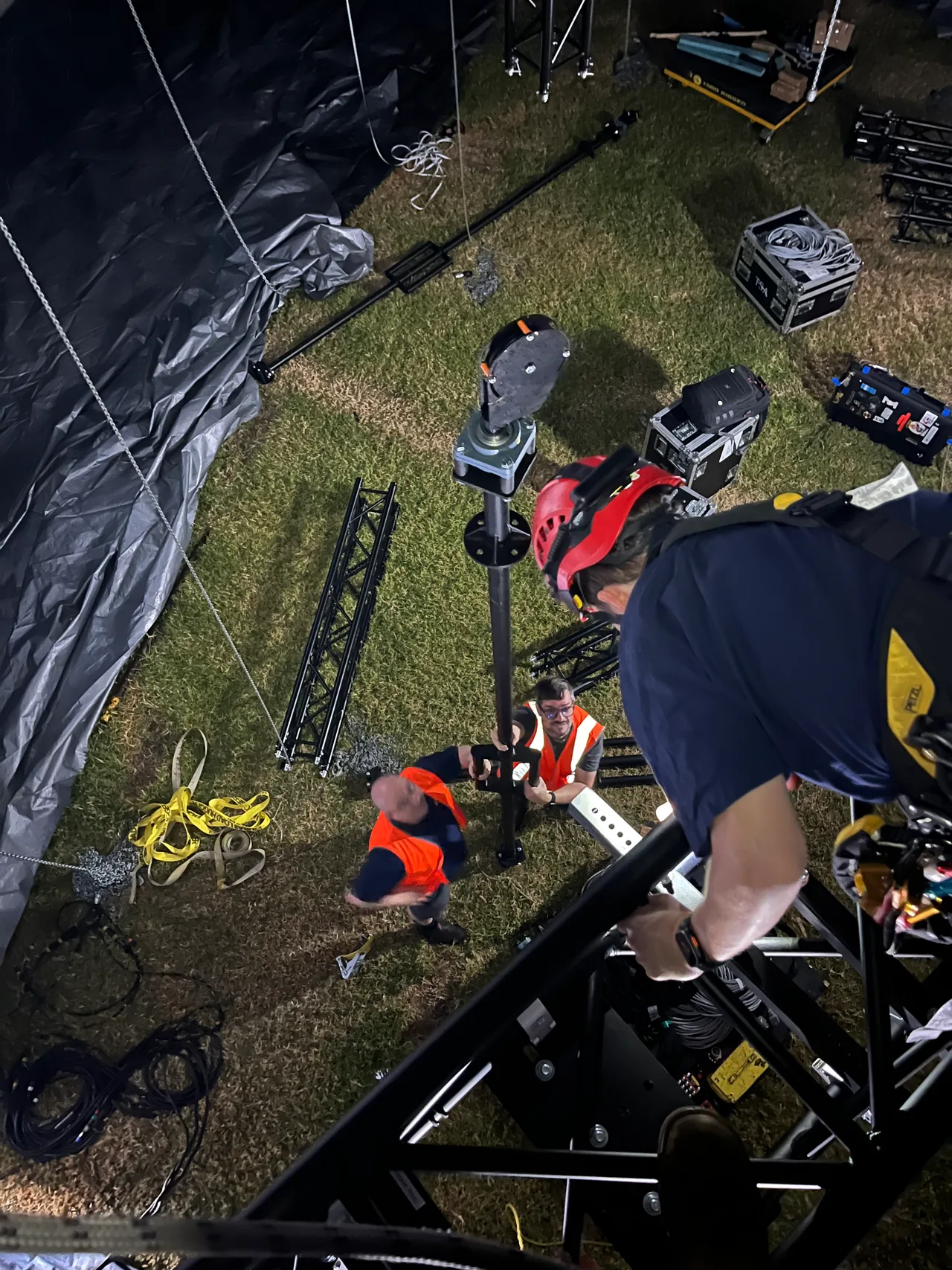 Crew assembling a winch spindle head on a mast at night, from the truss tower