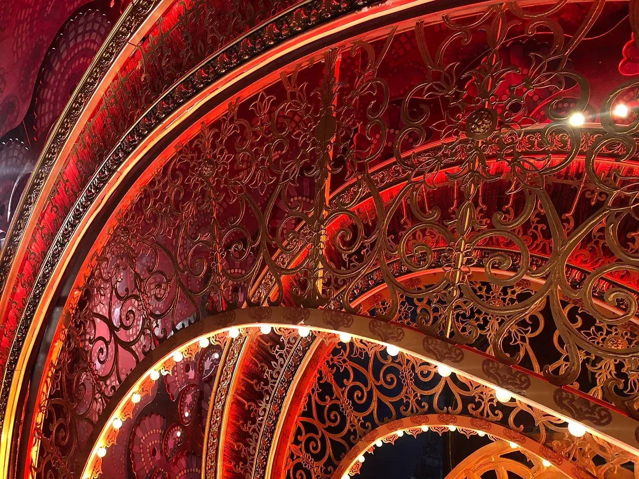 Nested Moulin Rouge portal arches lit with chase bulbs, gold filigree over red. Photo: TSA.