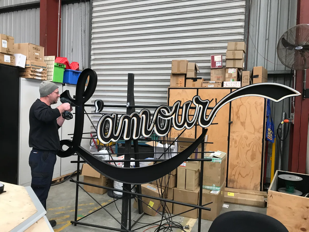 Fabricator drilling the L'amour sign set piece on its steel frame in the scenic workshop