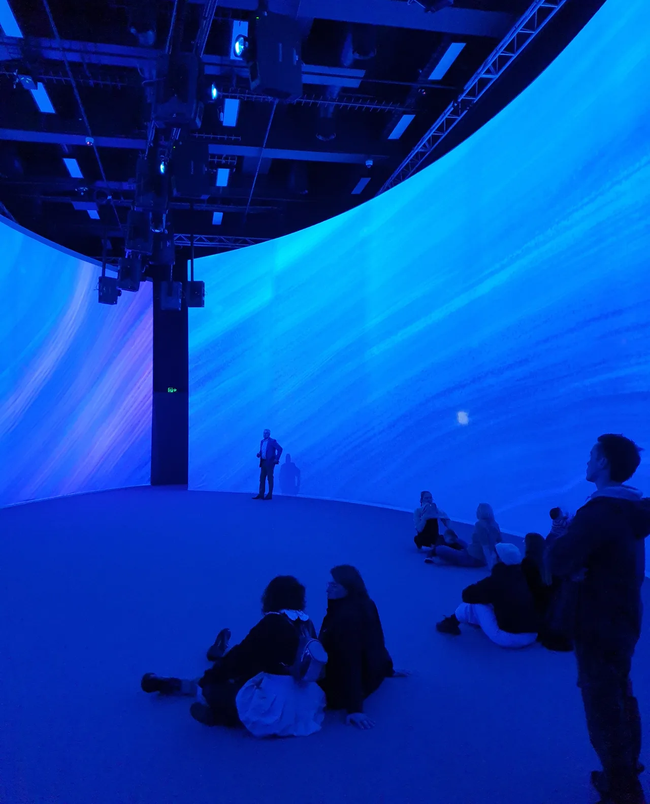 Visitors seated inside a curved cyclorama projection room bathed in blue ocean imagery