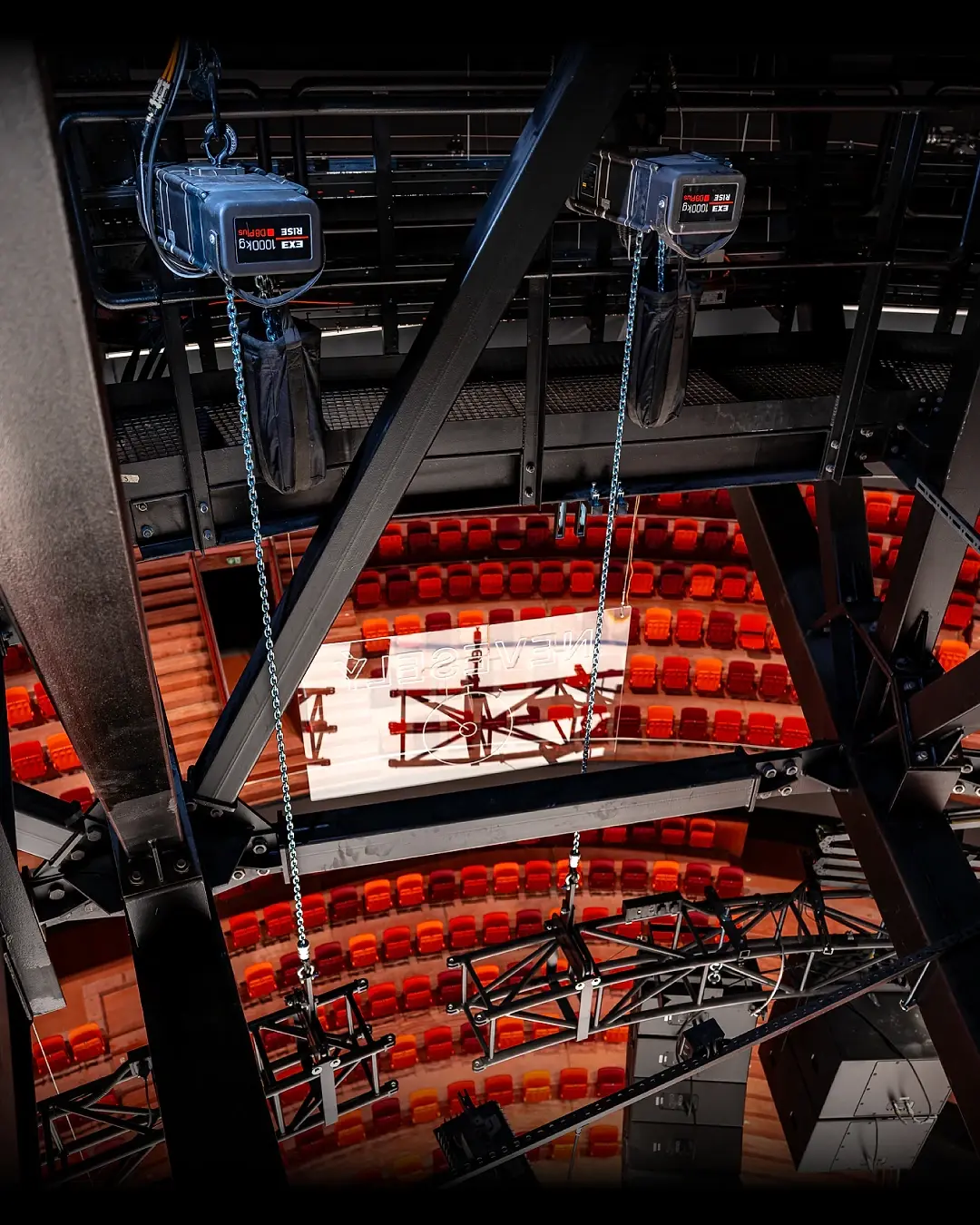 Two EXE Rise chain hoists flown from overhead steel above a red-seated auditorium