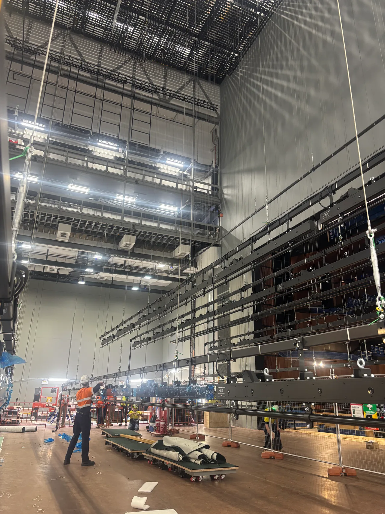 Rows of lighting bars and battens rigged on wire lines in a fly tower during a venue fit-out