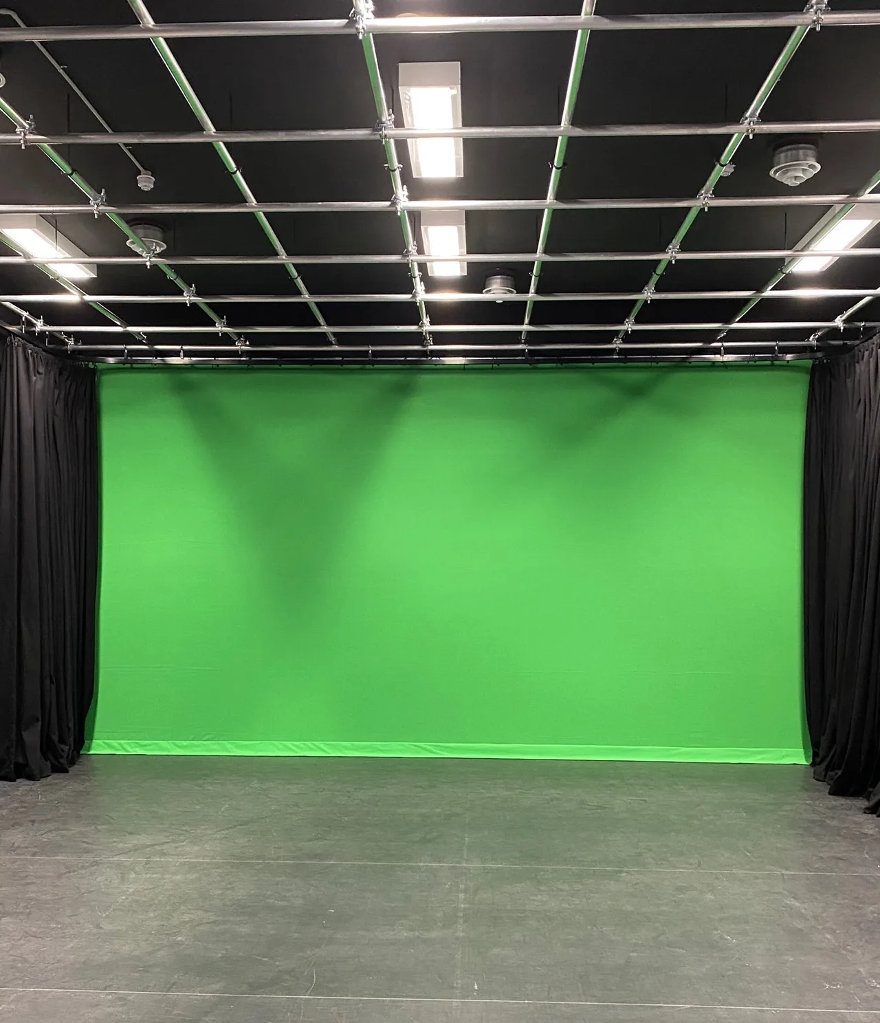 A green screen cyclorama with black masking drapes under a pipe grid in a studio fit-out