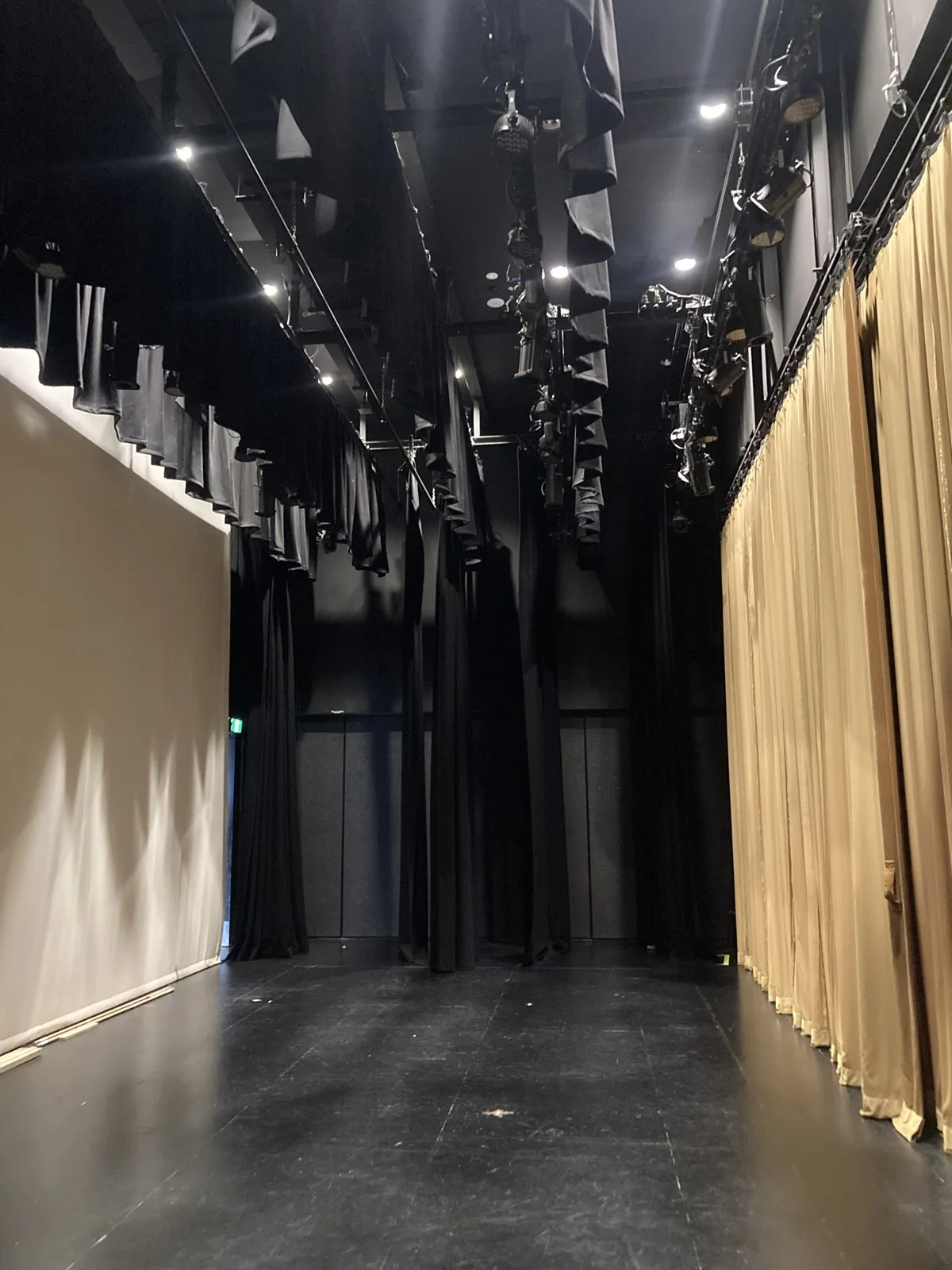 A school stage with black wool masking, gold front tabs and overhead lighting bars